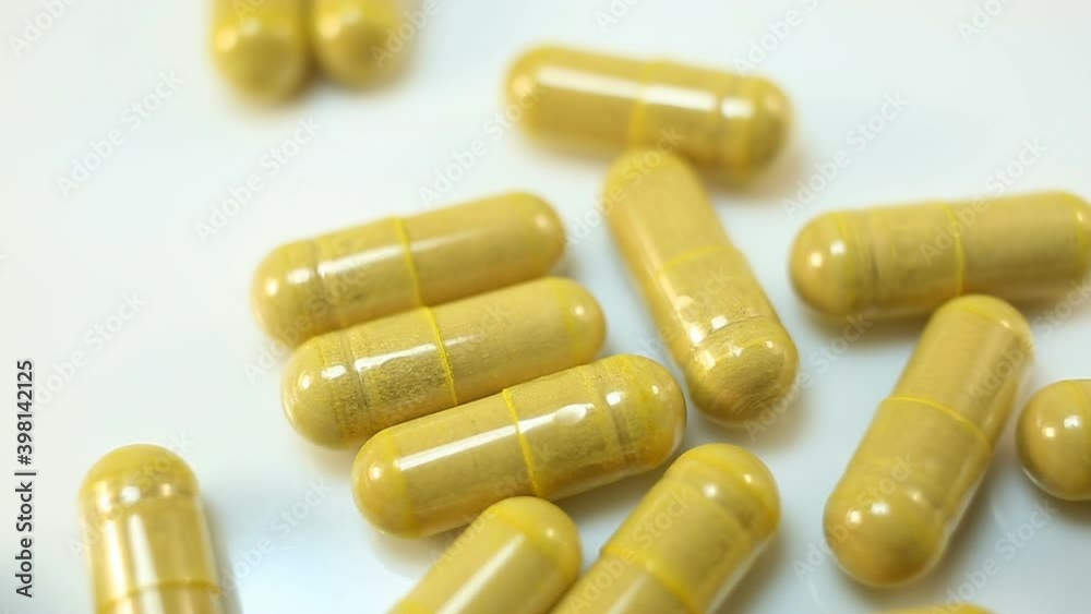 Bright yellow capsules with the drug are poured and rolled down on a white background. Extreme close-up, real time, medicine, pharmacy Bright yellow capsules with the drug are poured and rolled down on a white background. Extreme close-up, real time, medicine, pharmacy