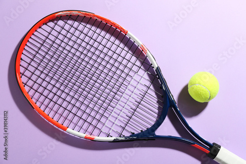 Tennis racket and ball on violet background, flat lay. Sports equipment