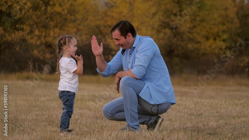 Dad and little daughter say hello. The child claps his father on the palm, a happy family plays in the park. Teamwork of baby and daddy. A fun outdoor game, dad loves his baby. Healthy family