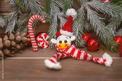 knitted toy white bull head in christmas cap and scarf with fir branches and decor on wooden brown background