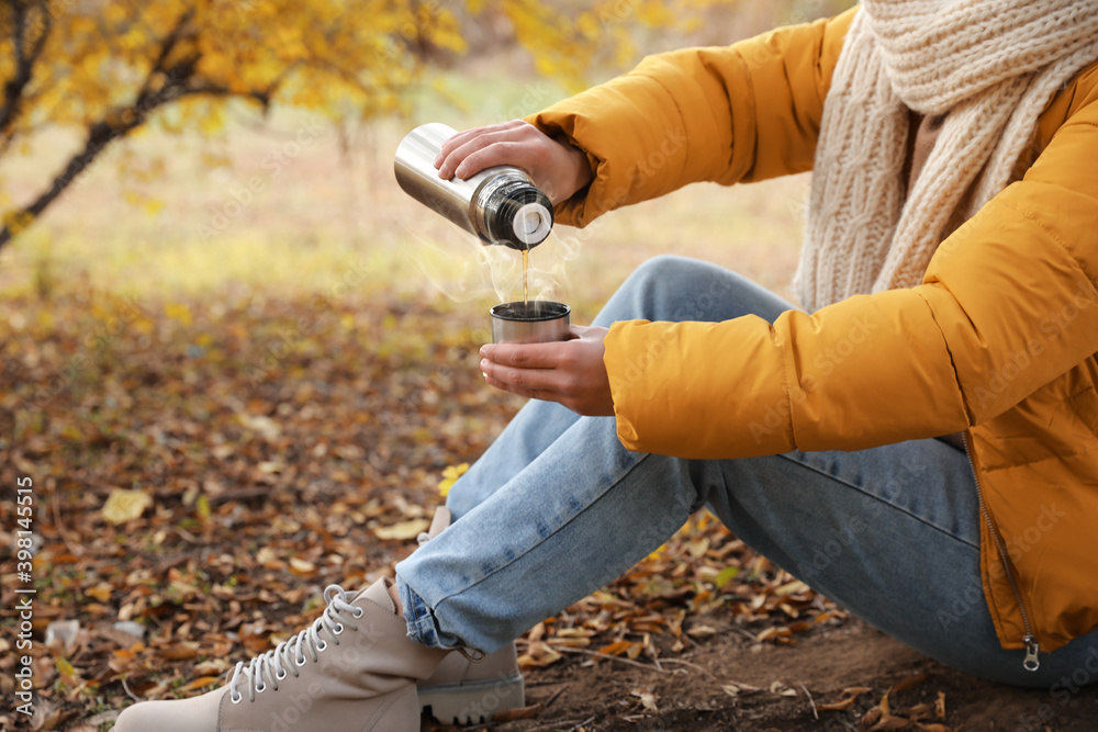 Fototapeta premium Woman with thermos sitting on ground outdoors, closeup