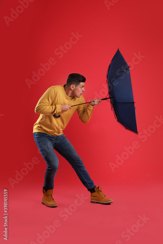 Fotografie Emotional man with umbrella caught in gust of wind on red background