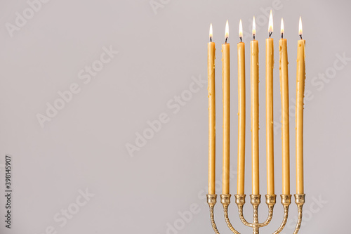 Golden menorah with burning candles on light grey background  space for text