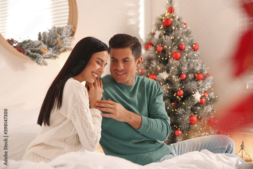 Happy couple on bed near Christmas tree at home