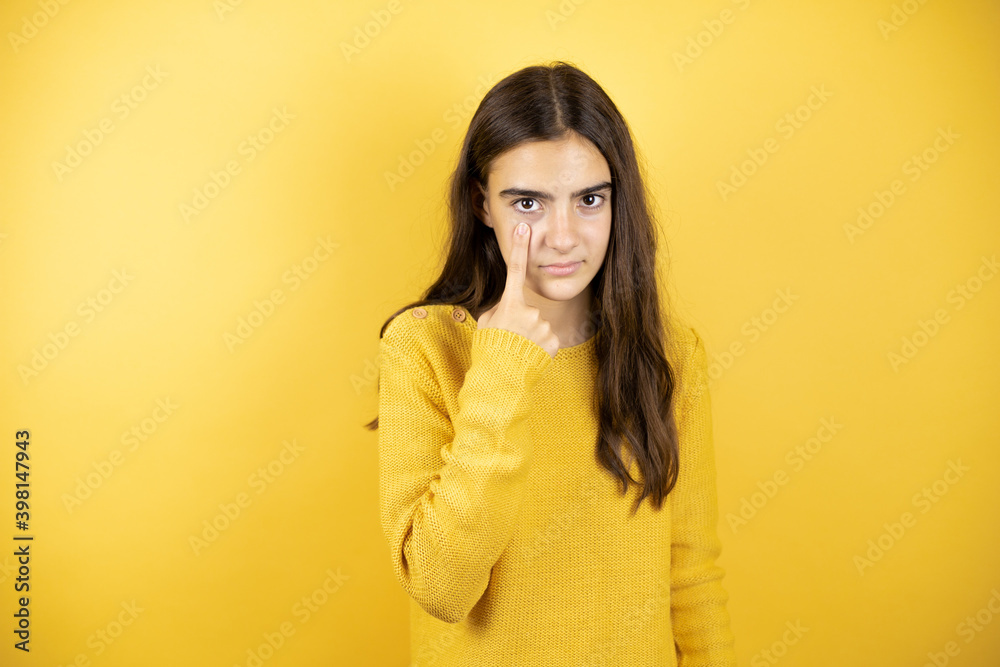 Pretty girl wearing a yellow sweater standing over isolated yellow background Pointing to the eye watching you gesture, suspicious expression Pretty girl wearing a yellow sweater standing over isolated yellow background Pointing to the eye watching you gesture, suspicious expression
