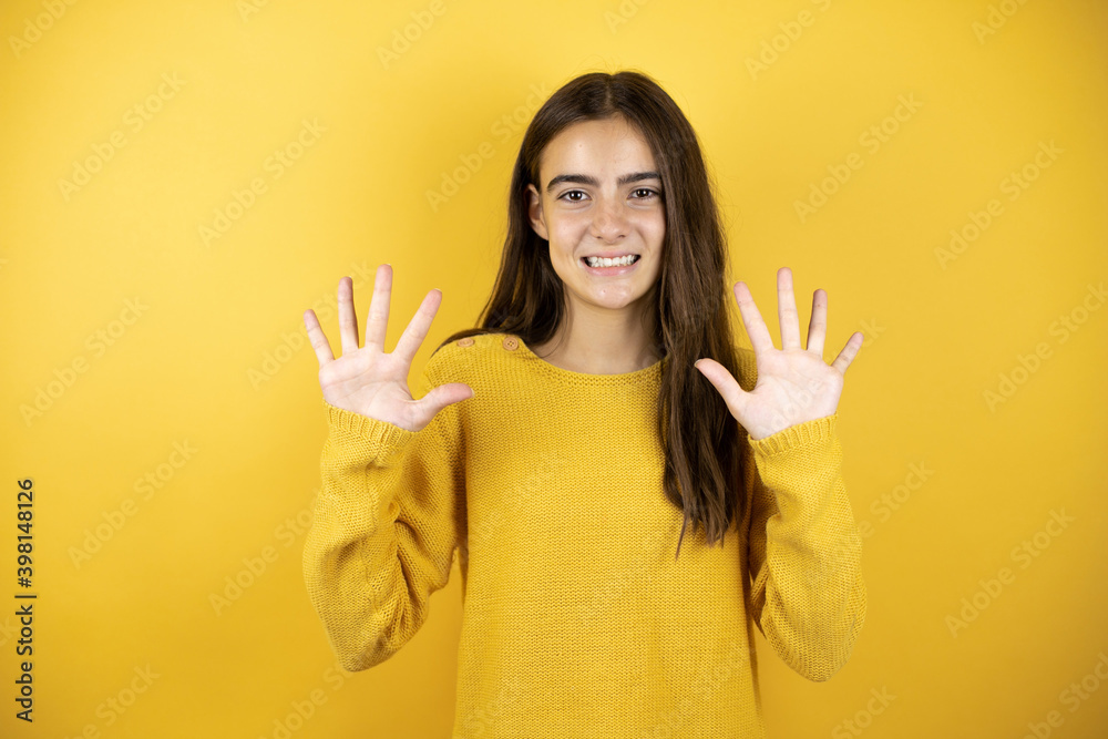 Pretty girl wearing a yellow sweater standing over isolated yellow background showing and pointing up with fingers number ten while smiling confident and happy Pretty girl wearing a yellow sweater standing over isolated yellow background showing and pointing up with fingers number ten while smiling confident and happy