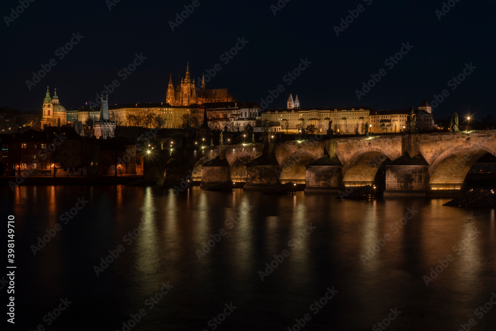 . prague castle and charles bridge and st. vita church lights from street lights are reflected on the surface of the vltava river in the center of prague at night in the czech republic
