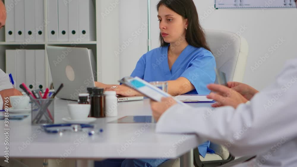 Portrait of nurse typing on laptop during brainstorming and looking at camera smiling sitting on desk in hospital office, conference room. Specialist in lab coat writing on notepad in medical clinic. Portrait of nurse typing on laptop during brainstorming and looking at camera smiling sitting on desk in hospital office, conference room. Specialist in lab coat writing on notepad in medical clinic.