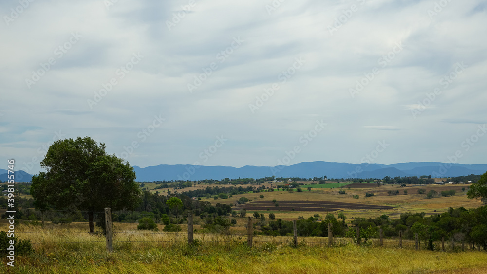 Panoramic rural landscape with fence in the foreground and blue tinged mountains in the distance. Overcast sky. Scenic Rim, Queensland, Australia.