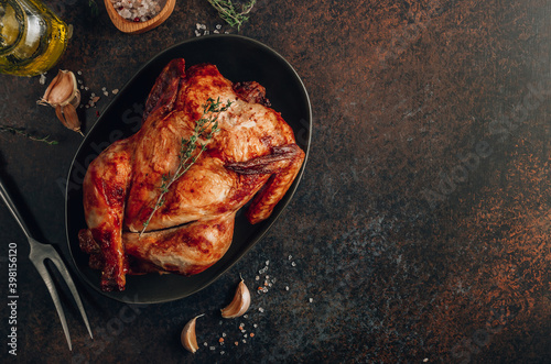 Homemade chicken roasted with thyme, garlic on a black board on a dark table.