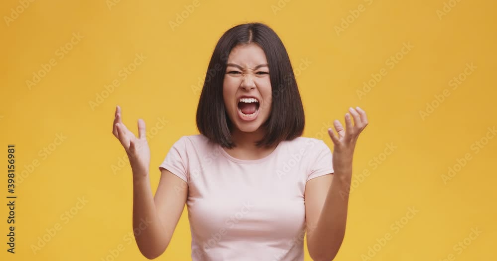 Young furious asian woman screaming loud and shaking hands, feeling rage and anger, orange studio background Young furious asian woman screaming loud and shaking hands, feeling rage and anger, orange studio background