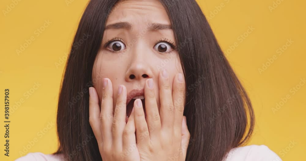 Close up portrait of young afraid asian lady, feeling afraid and panicked , orange studio background Close up portrait of young afraid asian lady, feeling afraid and panicked , orange studio background
