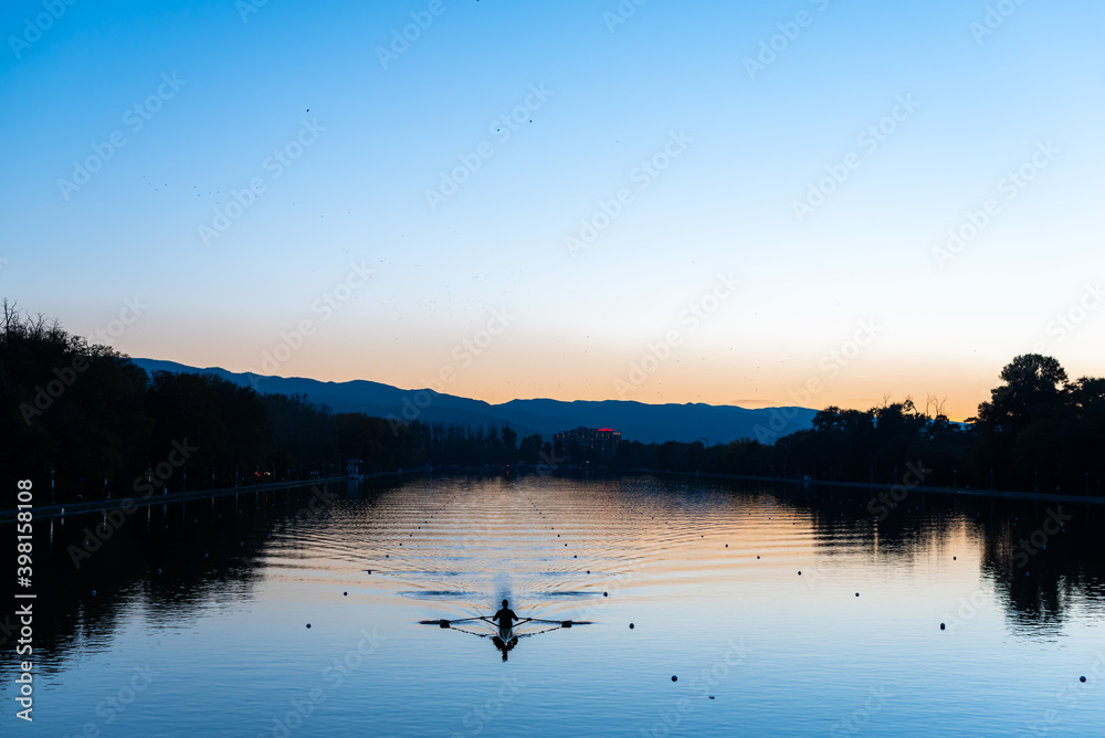 Lonely rowing boat sports in long canal training in calm sunset water with reflections and vibrant colors in Plovdiv, Bulgaria