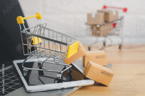Shopping cart with laptop on wood table in office background.Easy shopping with finger tips for consumers.Online shopping and delivery service concept.