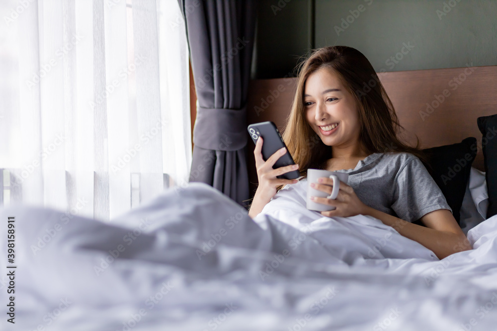 Beautiful long hair women play smartphone on the bed while hold a glass in her left hand. Beautiful long hair women play smartphone on the bed while hold a glass in her left hand.