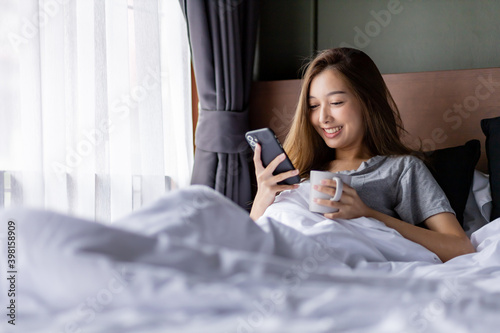Beautiful long hair women play smartphone on the bed while hold a glass in her left hand.