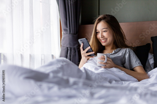 Beautiful long hair women play smartphone on the bed while hold a glass in her left hand.