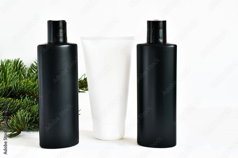 Christmas cosmetics products. Black and white blank bottles and fir tree branches on a white background. Moisturizing skincare product in the winter season. Advertising cosmetics product. Christmas cosmetics products. Black and white blank bottles and fir tree branches on a white background. Moisturizing skincare product in the winter season. Advertising cosmetics product.