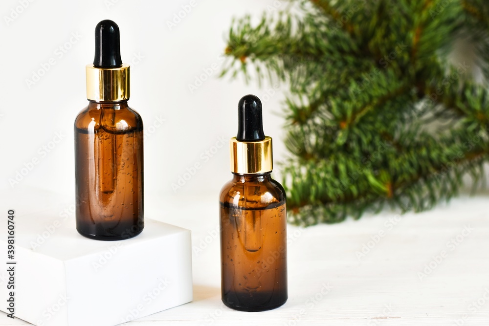 Fototapeta premium Two dropper oil bottles. Serum oil in glass bottles with a dropper with fir tree branches on a white background. Natural organic cosmetic, eco lotion, essence, serum. Copy space. Advertising.