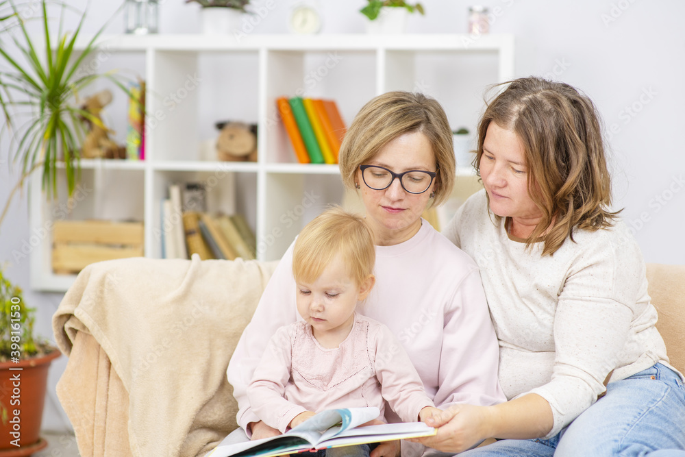 Female couple sitting on the sofa of their front room with their child, readding her a book Female couple sitting on the sofa of their front room with their child, readding her a book