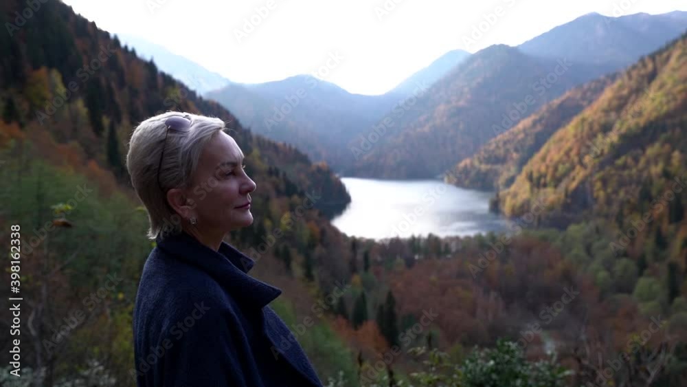 Portrait of a fair-haired middle-aged woman admiring in a tropical place in the mountains against the background of green trees and a lake, smiling. Portrait of a fair-haired middle-aged woman admiring in a tropical place in the mountains against the background of green trees and a lake, smiling.