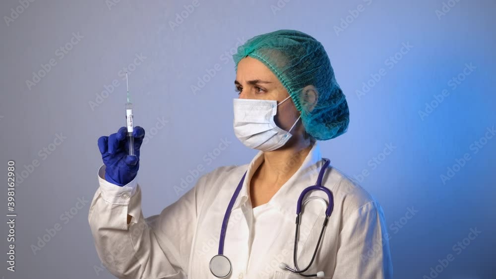 Female Doctor in Protective Medical Mask and Blue Rubber Gloves Holding a Syringe with Coronavirus/COVID-19 Vaccine. Slow Motion. Healthcare, Safety and Sickness Prevention Against Viruses Female Doctor in Protective Medical Mask and Blue Rubber Gloves Holding a Syringe with Coronavirus/COVID-19 Vaccine. Slow Motion. Healthcare, Safety and Sickness Prevention Against Viruses