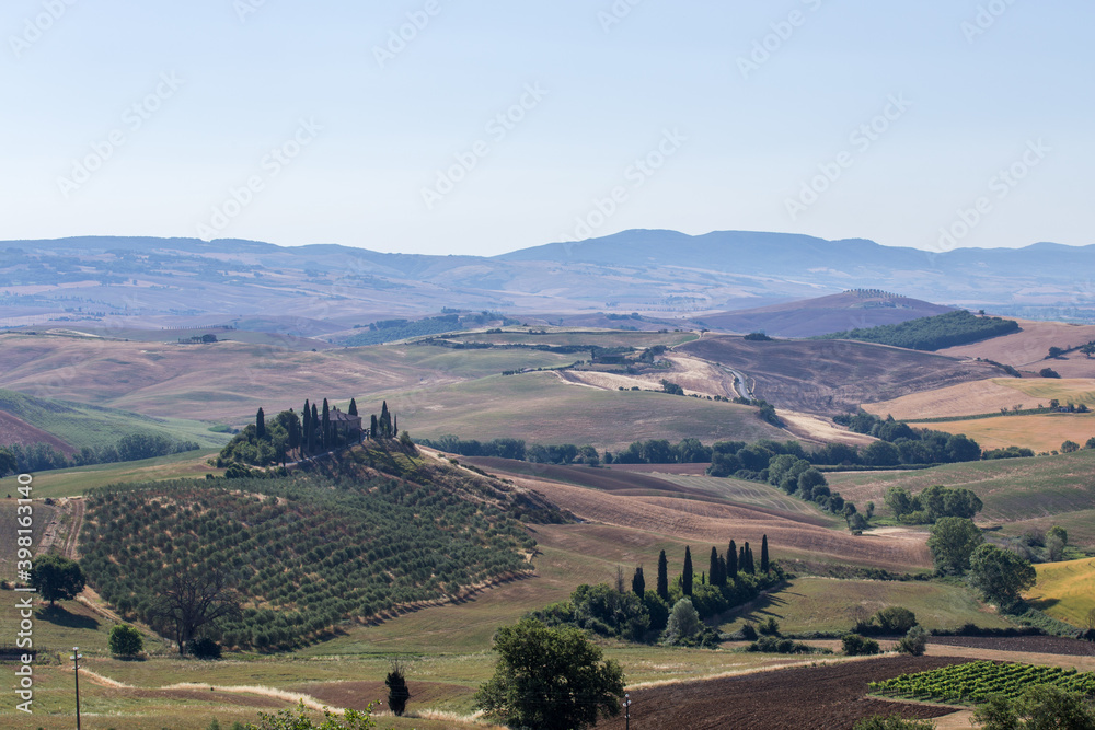 Summer rural landscape with trees, fields, meadows and hills in the background, of the traditional farm house in Tuscany, Italy