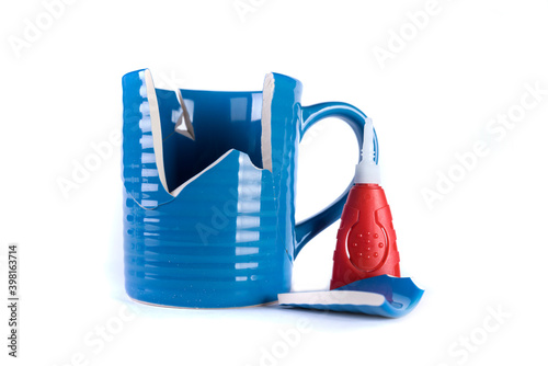 Broken blue mug with a glue tube and a shattered piece laying next to it