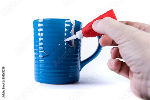 Hand appyling glue to a crack in an almost repaired cup photo