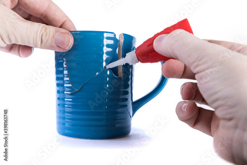 Hand holding a broken piece while applying glue to a hole in a cup photo