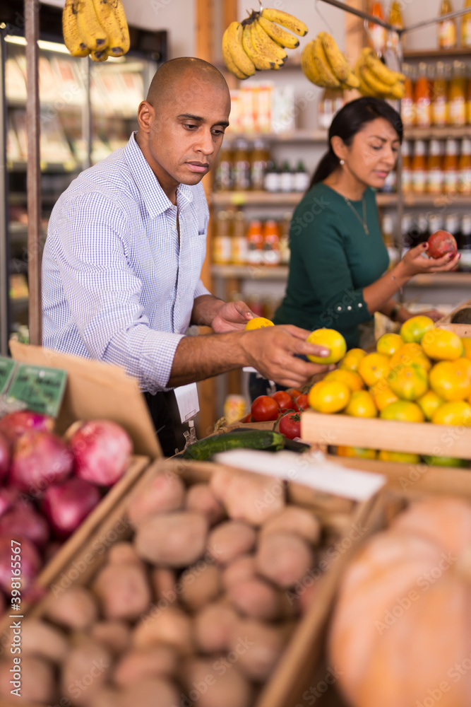 Positive hispanic man looking for fresh tangerines in vegetable and fruit section of supermarket