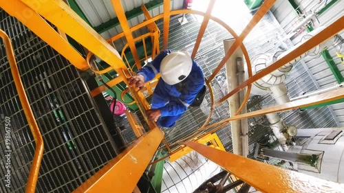 An engineer climbed a vertical ladder to inspect the work in the factory. Oil refinery working concept
