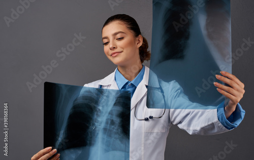 A woman in a medical gown examines X-rays on a gray background