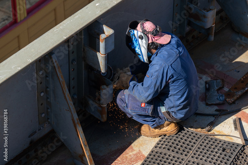 Male worker from behind on a construction site, welding the wall of a ship being restored, closeup.