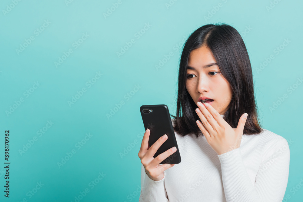Portrait female anxious scared on the phone seeing bad news, Young beautiful Asian woman surprised shocked with mobile phone close mouth with palm, studio shot isolated on a blue background Portrait female anxious scared on the phone seeing bad news, Young beautiful Asian woman surprised shocked with mobile phone close mouth with palm, studio shot isolated on a blue background