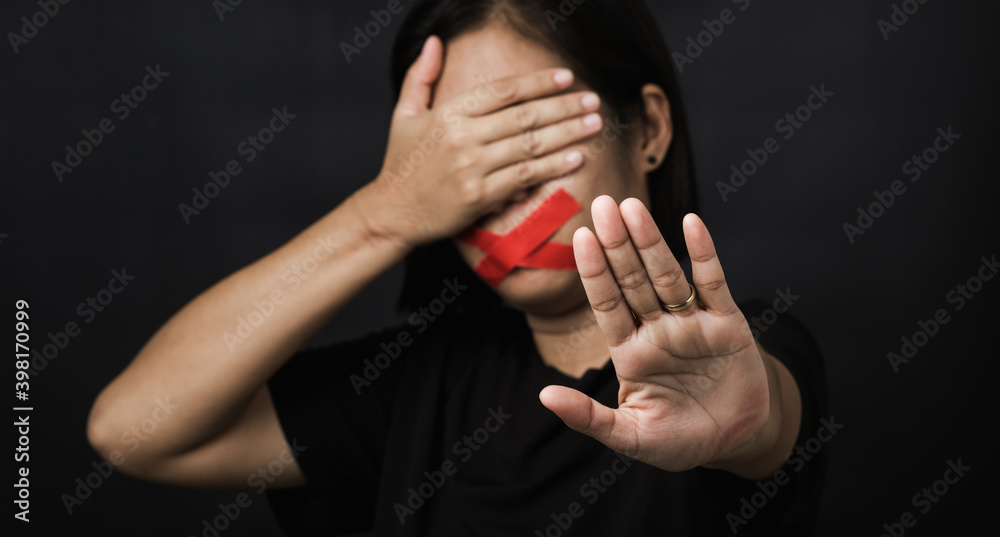 Woman blindfold wrapping mouth with red adhesive tape and show hand sign stop abusing violence and abuse on black background, Human trafficking and abuse, International Human Rights day