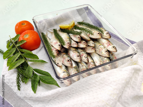 Fresh Indian Oil Sardine decorated with tomatoes and curry leaves on a glass bowl.White Background,Selective Focus. photo