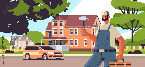 professional repairman in uniform holding hammer and toolbox home maintenance repair service concept cottage house building exterior full length horizontal vector illustration