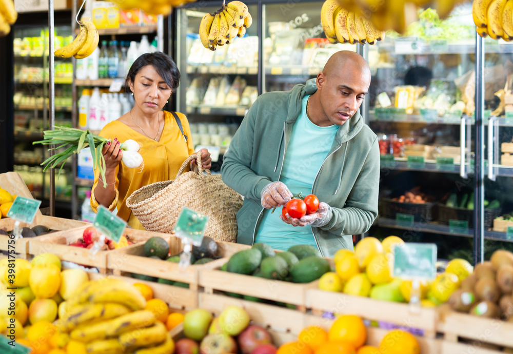 Smiling latin american family couple looking for fresh fruits and vegetables in food store