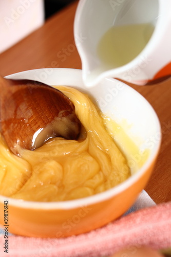 Pouring oil to an egg yolk. Making mayonnaise with a wooden spoon.