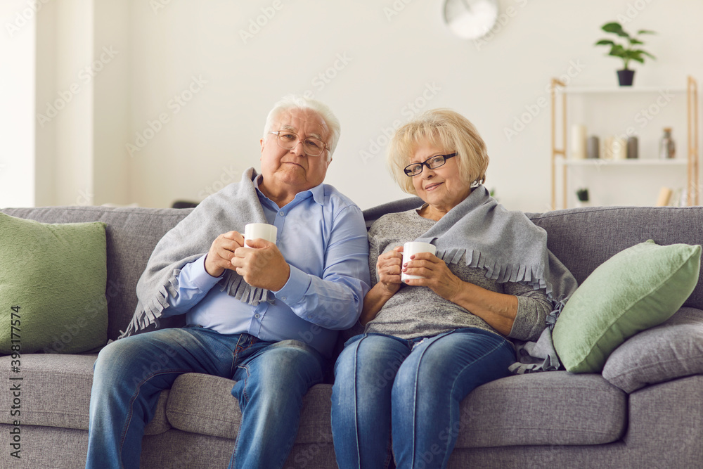 Portrait of a senior couple wrapped in a plaid sitting on the couch and drinking hot tea. Portrait of a senior couple wrapped in a plaid sitting on the couch and drinking hot tea.
