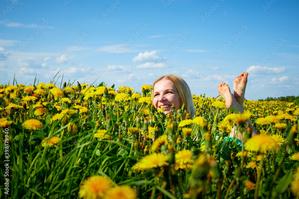 Pretty woman on a field with green grass and yellow dandelion flowers in a sunny day. Girl on nature with yellow flowers and blue sky. Pretty woman on a field with green grass and yellow dandelion flowers in a sunny day. Girl on nature with yellow flowers and blue sky.