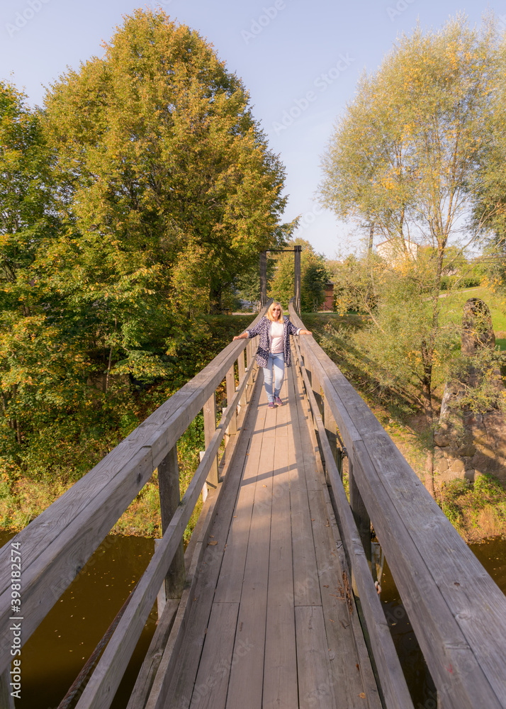 a wooden bridge over the river, a silhouette of a woman on the bridge, trees and shrubs in the background a wooden bridge over the river, a silhouette of a woman on the bridge, trees and shrubs in the background