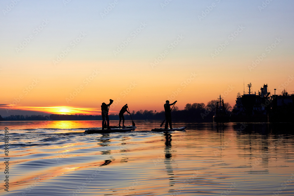 Silhouettes of children rowing on supboards at sunset in winter