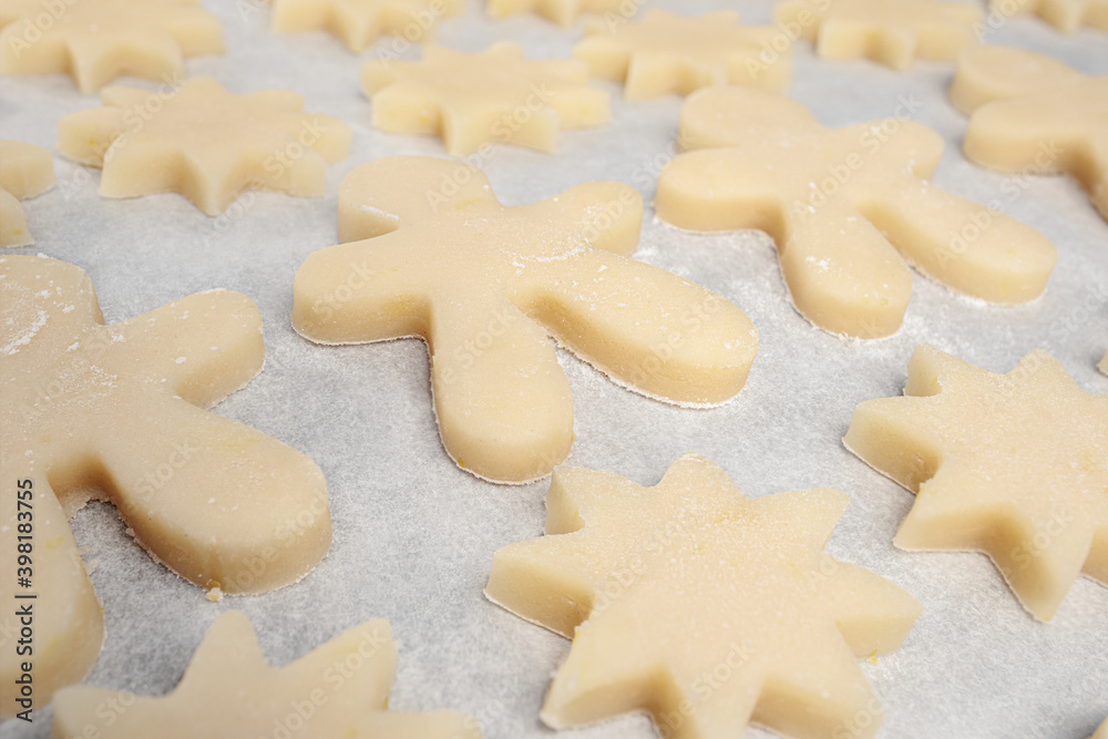 Many short bread sugar cookie on parchment paper, ready to be baked. Close up of cut out biscuits in star and gingerbread man shapes. Traditional Swiss Christmas cookie recipe Mailaenderli.