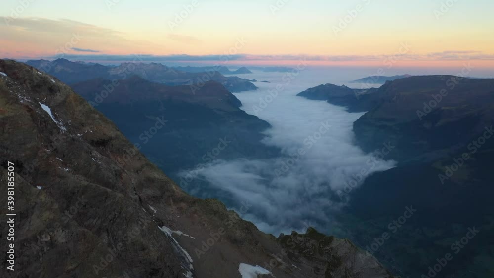 Drone shot moving sideways to the right. Small frozen river of ice runs down the side of the mountain peak to the glacier near Gleckstein hut in Switzerland. Colorful sunrise with a misty valley. Drone shot moving sideways to the right. Small frozen river of ice runs down the side of the mountain peak to the glacier near Gleckstein hut in Switzerland. Colorful sunrise with a misty valley.
