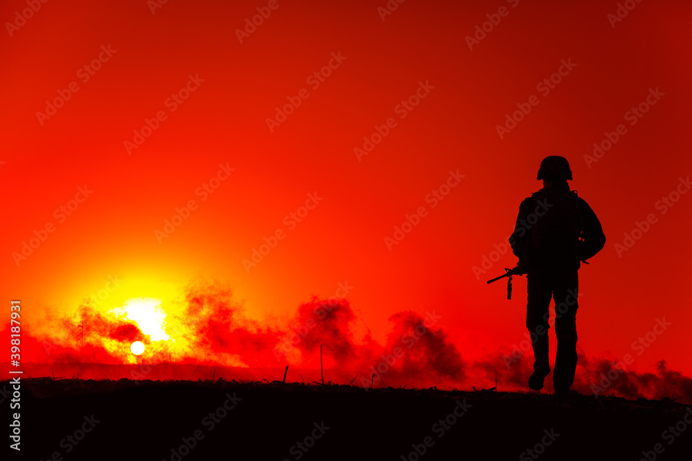 Silhouette of army soldier with service rifle walking to horizon with sunset and smoke. Special operations forces fighter, military company mercenary waking on battlefield after fight, patrolling area