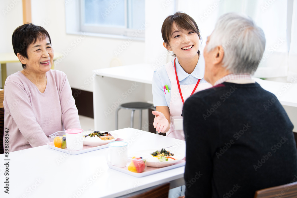 食事中の高齢の入居者たちと介護施設の女性職員 食事中の高齢の入居者たちと介護施設の女性職員