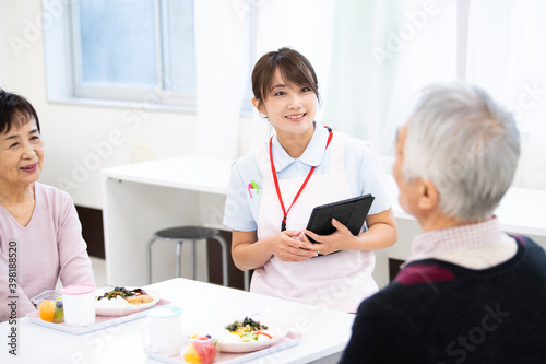 食事中の高齢の入居者たちと介護施設の女性職員 photo