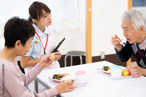 食事中の高齢の入居者たちと楽しく会話している介護施設の女性職員 photo